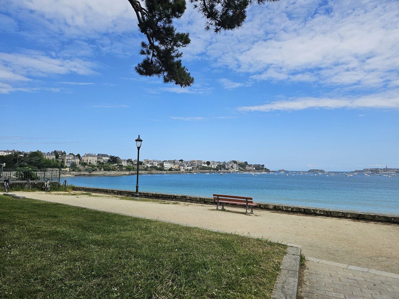 A lakeside promenade with a bench and hills across the water