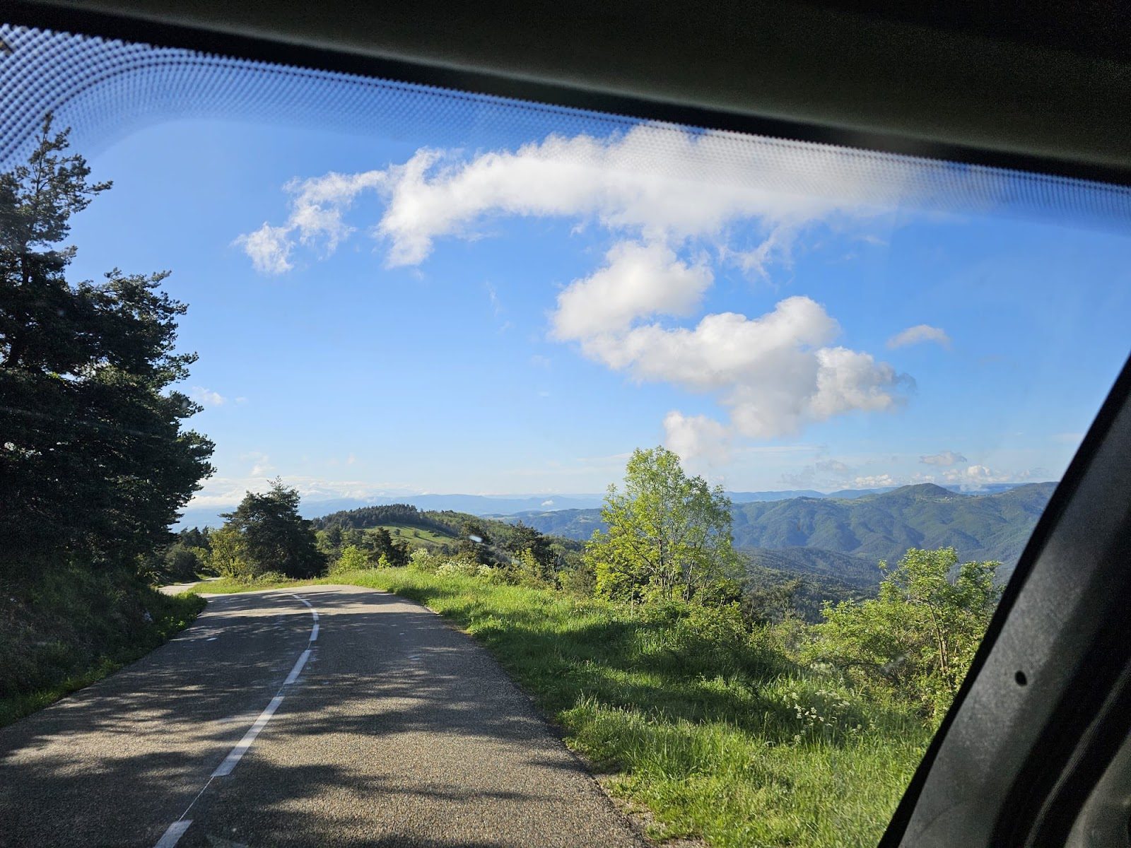 A road winding through green hills seen through a motorhome windscreen