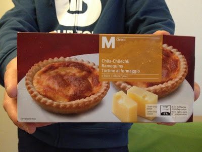 A shopper holding a box of Chäs-Chüechli, Swiss cheese tarts, in a Migros store